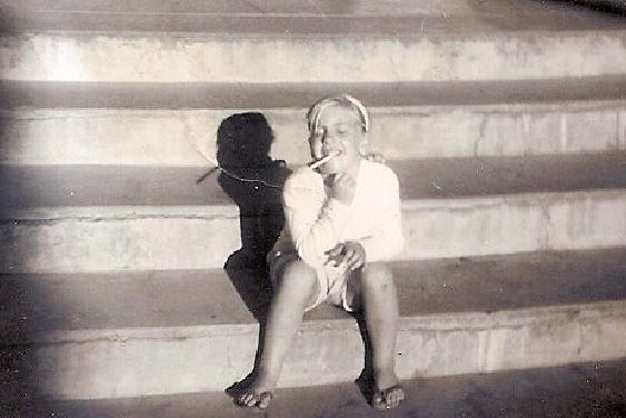 A little girl sitting on stone steps pretending to smoke a straw.