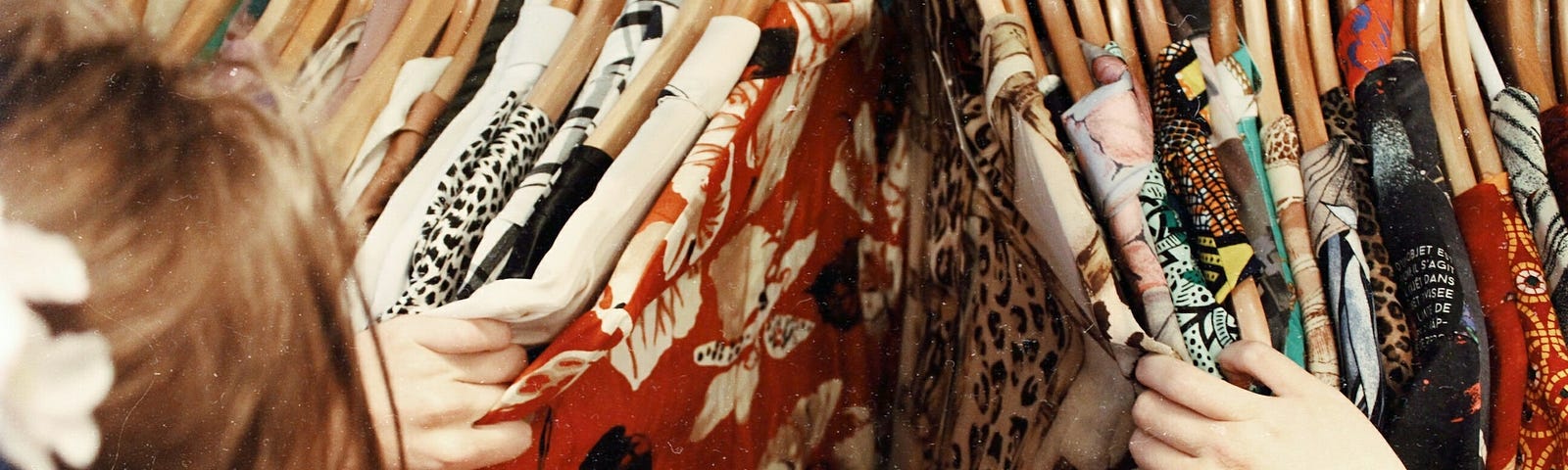 Woman with flower in hair sorting through clothing on wooden hangers of various, flashy patterns.