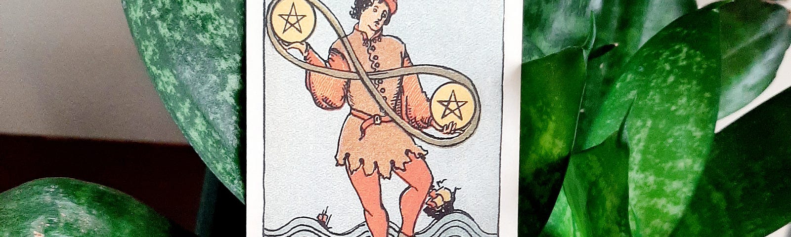 A man stands on one leg juggling two pentacle coins which are bound by an infinity loop. Boats sail on choppy waters behind him.