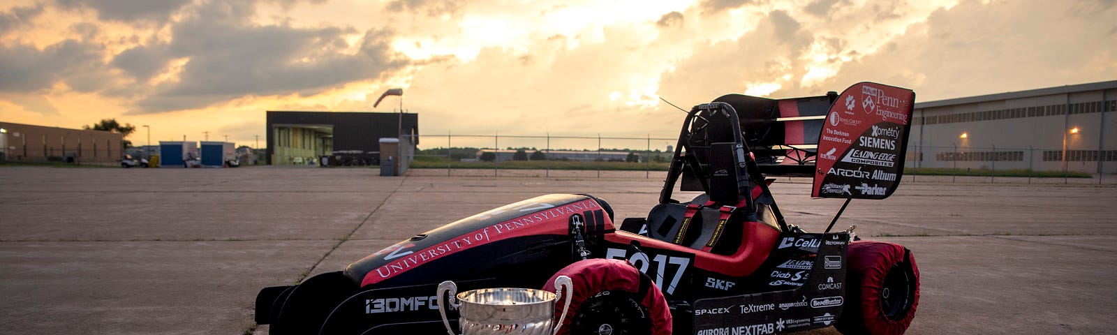 Penn Electric Racing’s REV5 car photographed after the Lincoln FSAE competition, with four trophies in the foreground.