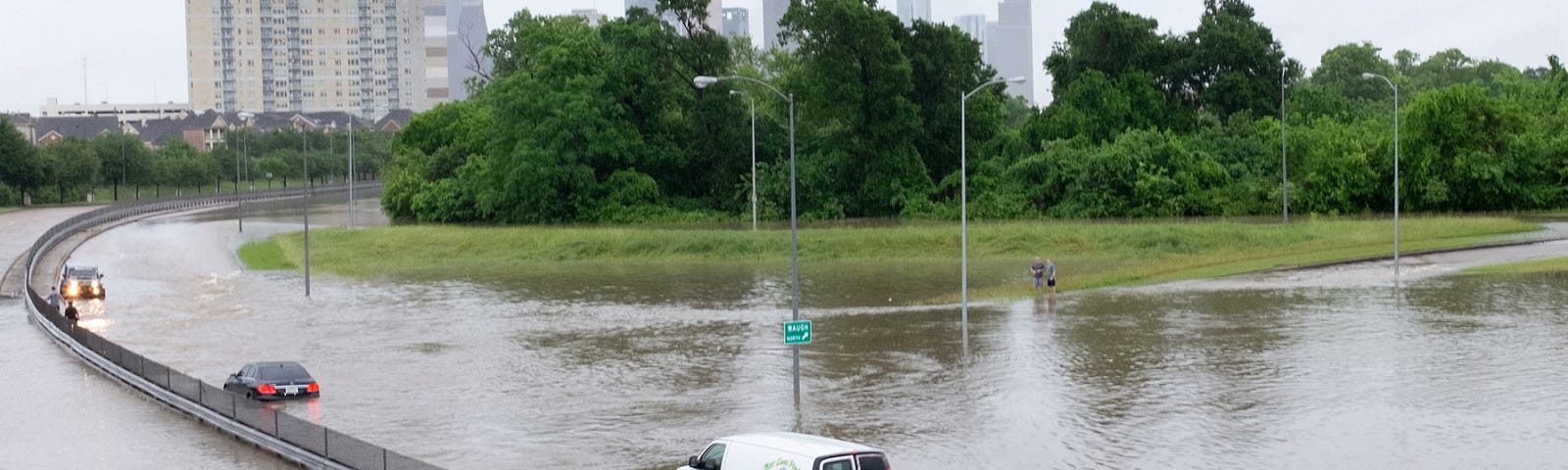 A van driving along a road in Houston, Texas is submerged in water during a flood event.