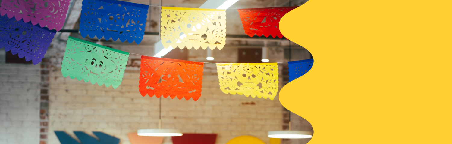 Colorful flags hang from the ceiling for Miro’s celebration of Hispanic Heritage Month. A bold yellow wavy graphic frames the photo on the righthand side.