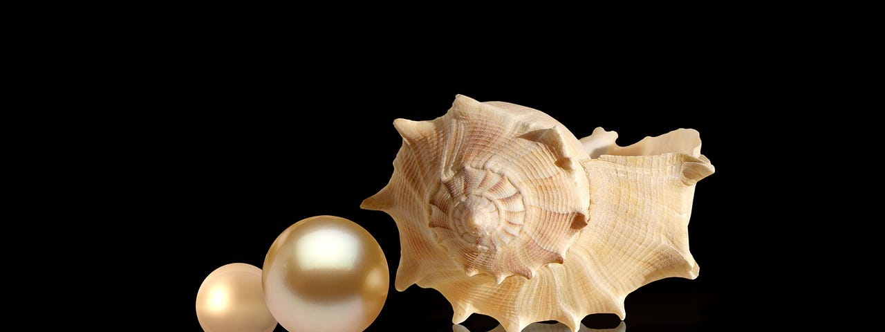 A white shell alongside two pearls, one large, one small reflected in a black background.