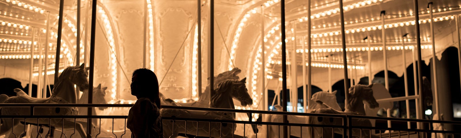 Girl standing in front of a carousel ride.