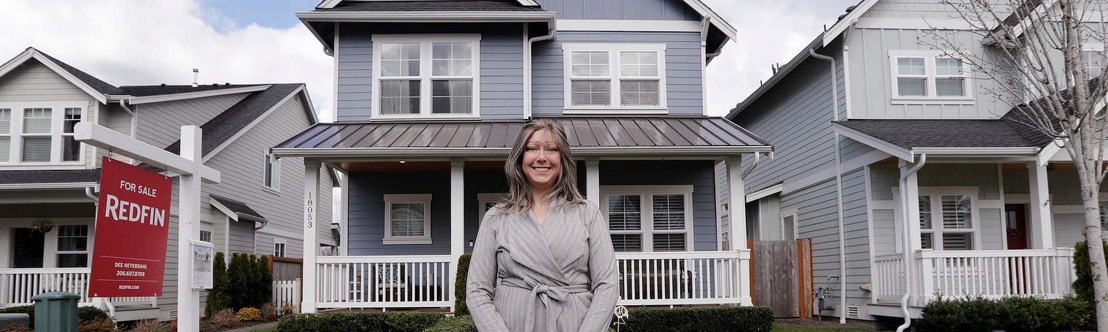 A Woman outside of a home with a “For sale” sign.