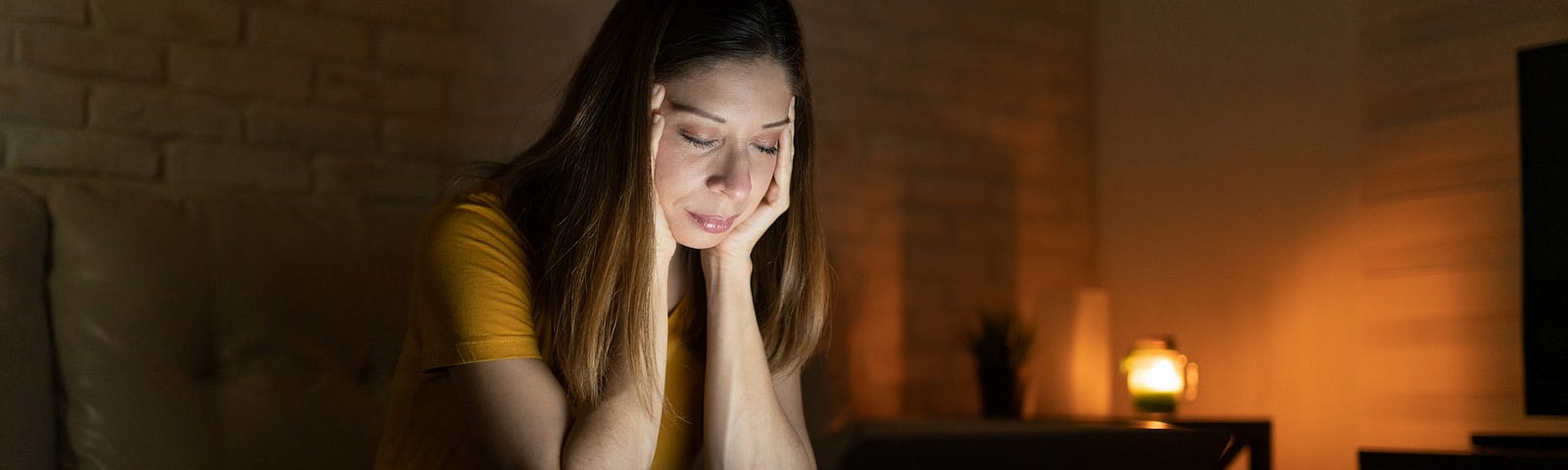 A sad-looking woman sitting at a laptop in the dark.