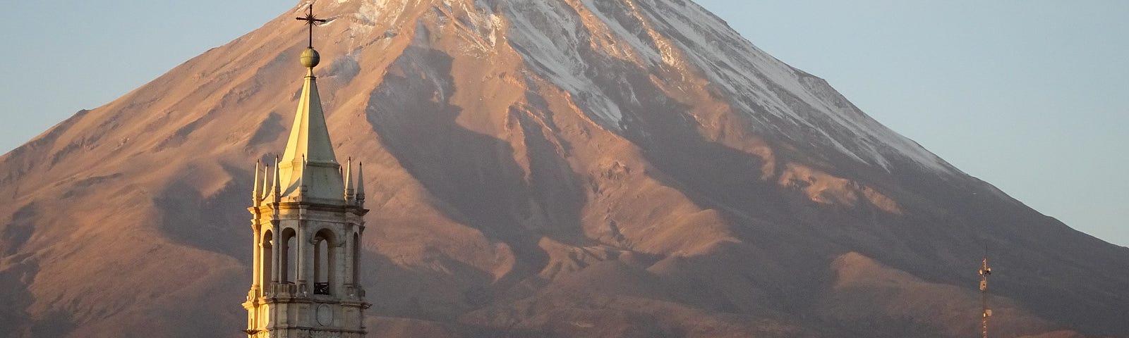 A church steeple infront of a large, slightly snow capped, mountain in Peru