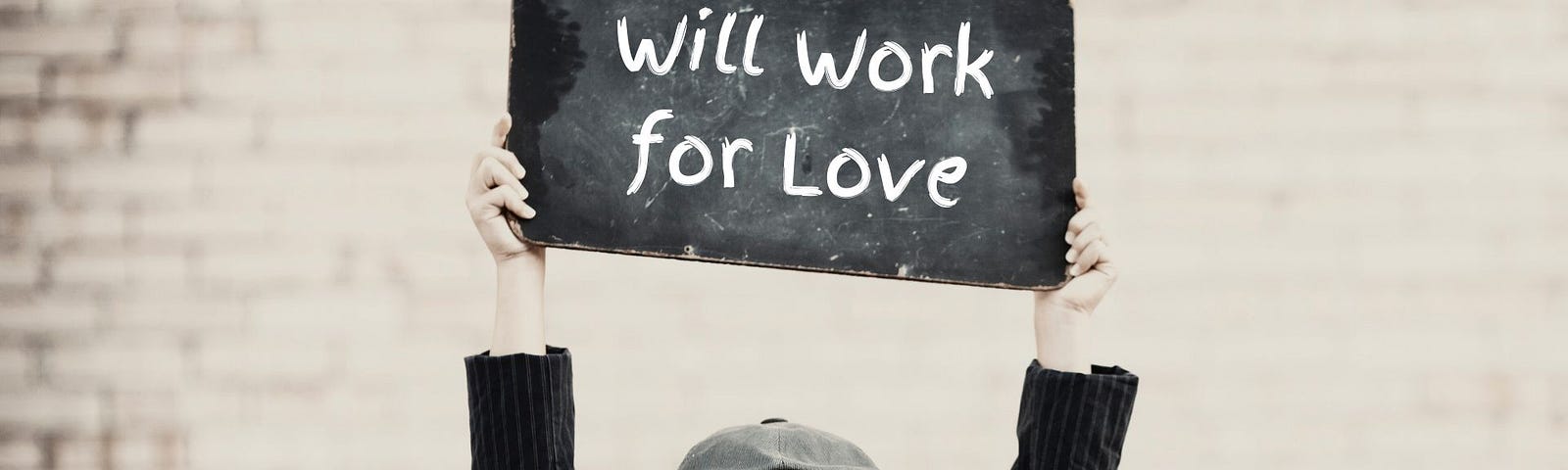 Photo of a boy holding up a small chalkboard. On the board is written the words, “Will work for love.”