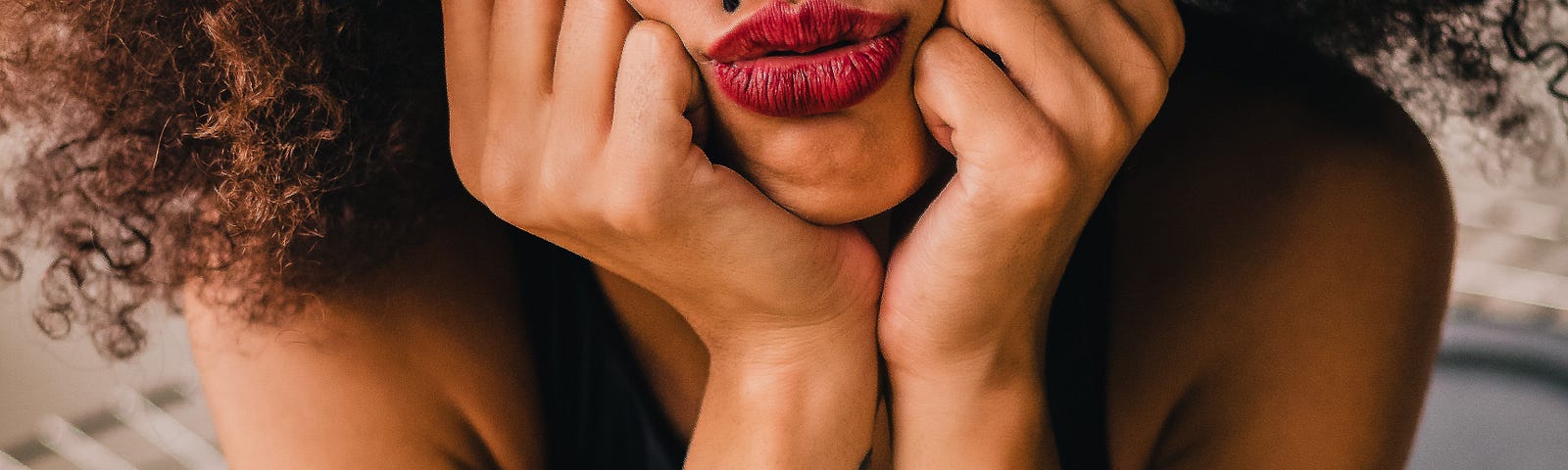 A black woman sitting with her face between her hands with pouting red lips.