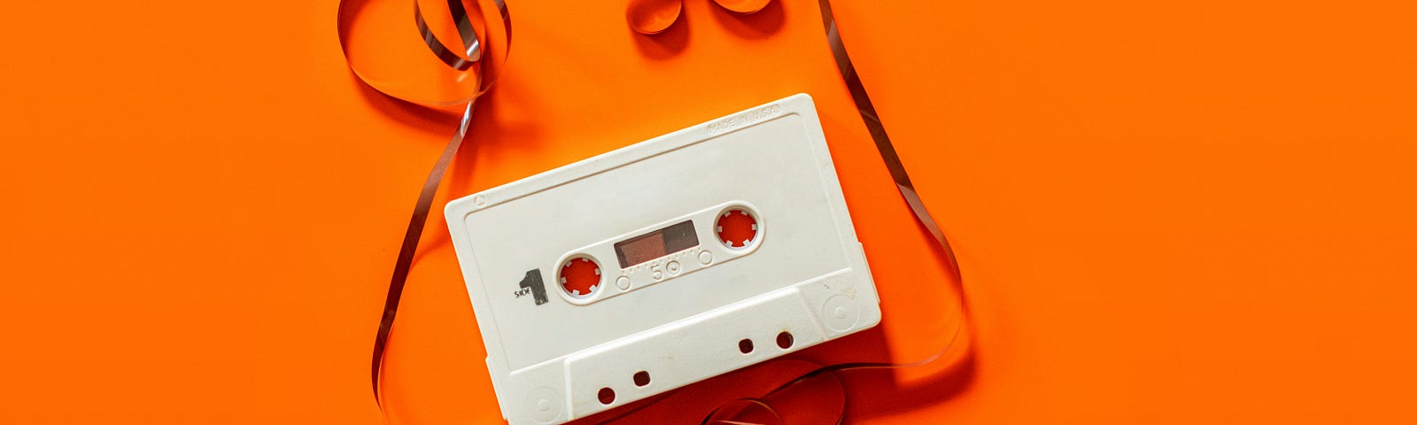 A cassette tape with unraveled tape spilling out of it against a bright orange background