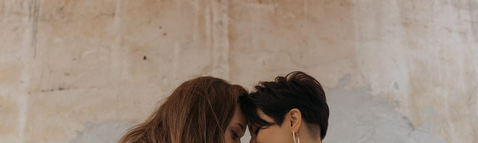 Two female presenting people sitting face to face with foreheads touching.