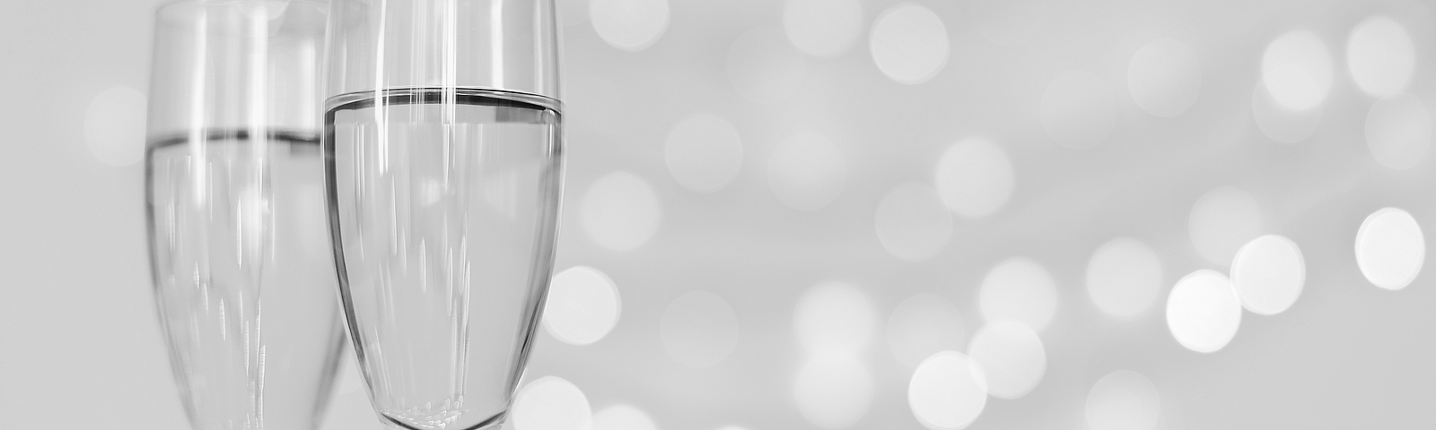 Black and White photo of two champaign glasses half filled in the left foreground against a champaign-colored background.