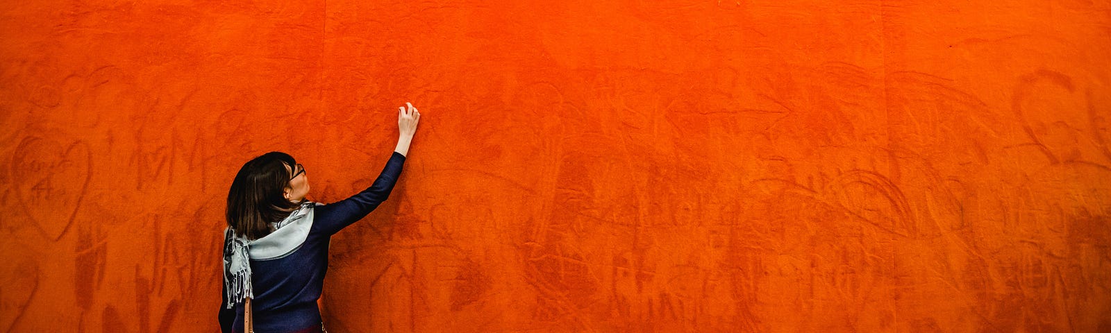 Woman writing on a bright orange wall.