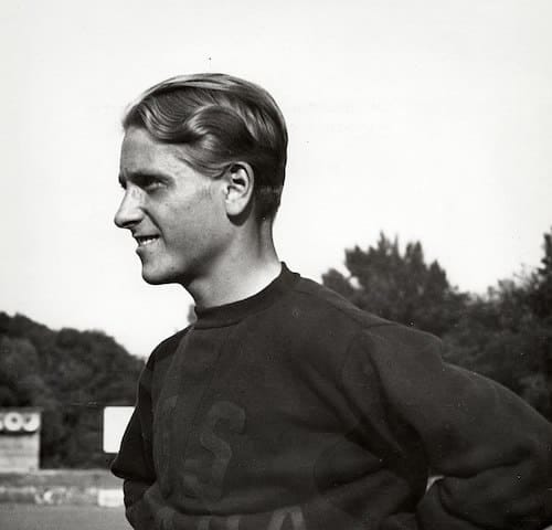 Zdeněk Koubek, standing on a sports field, wearing an athletic shirt, smiling, hands on his hips