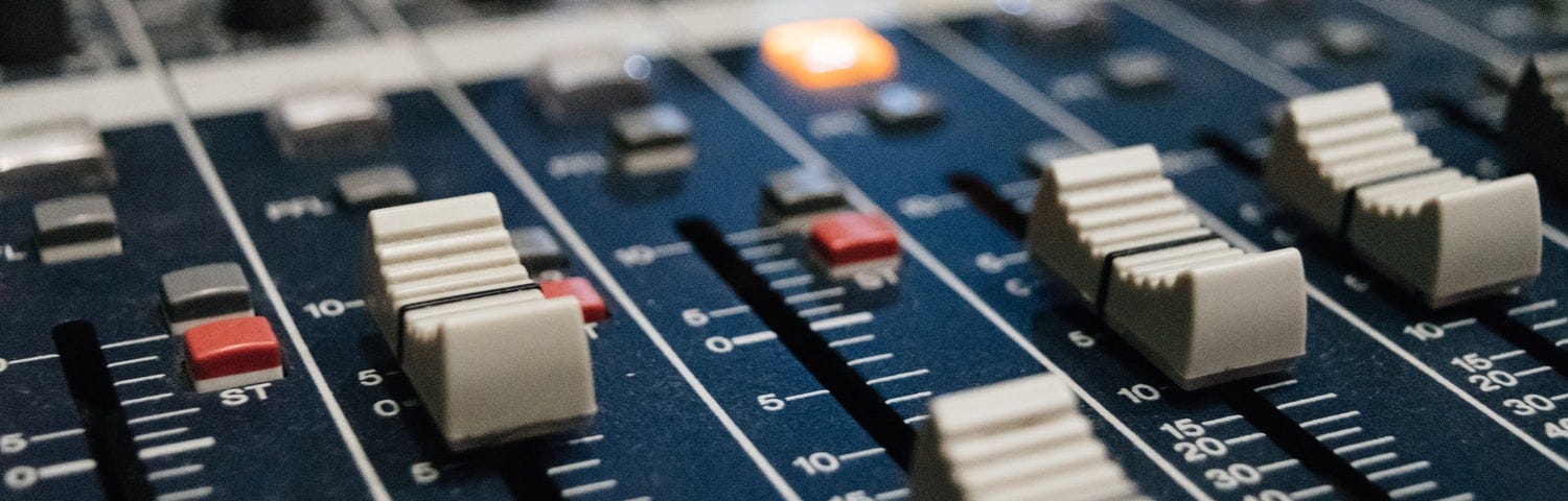 Knobs and faders on a music mixing panel.