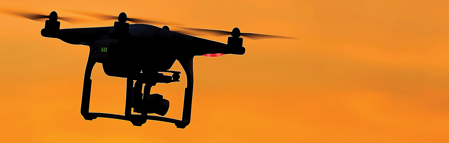 A silhouette of a drone flying in the sunset.