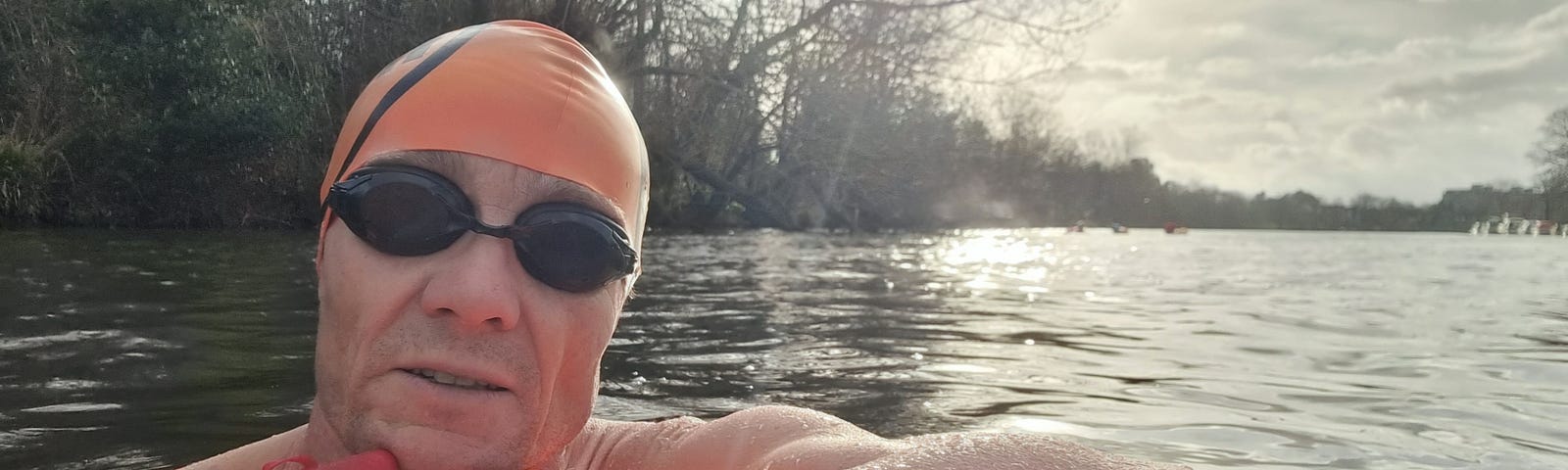 A selfie while swimming in the Thames, wearing goggles and an orange swim cap.