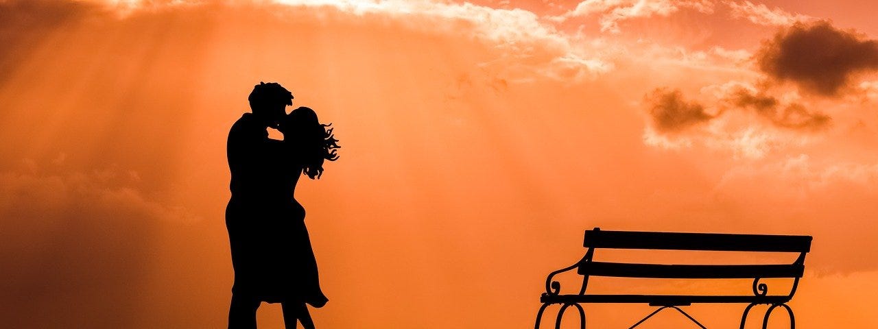 Image of the silhoutte of a couple kissing with the sunset as a background