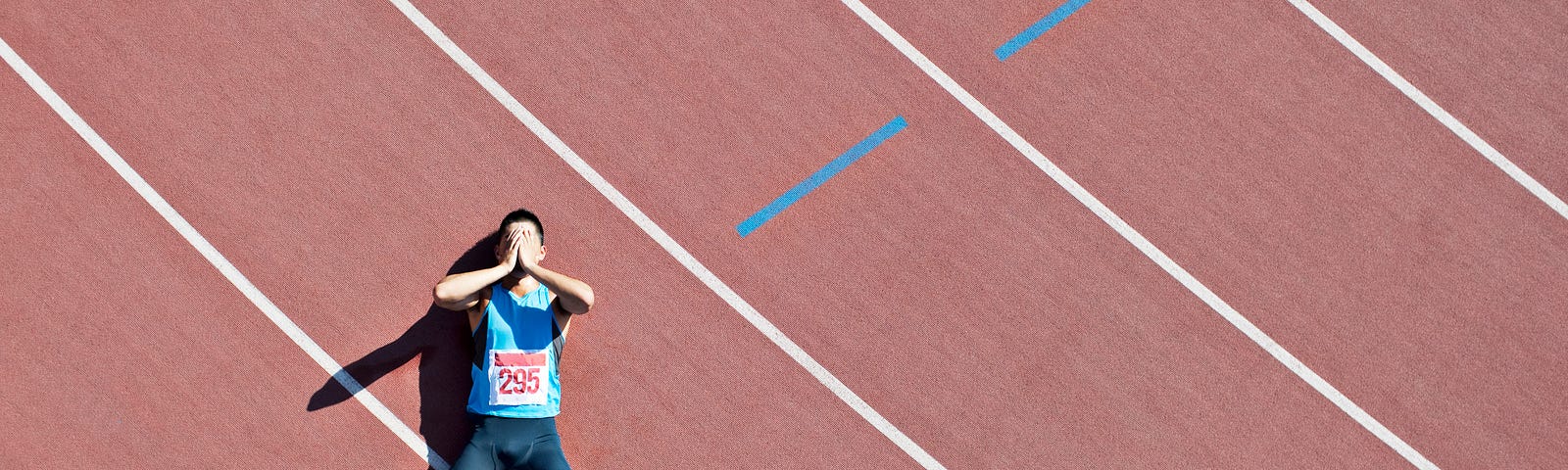 A tired runner lies down on a track.