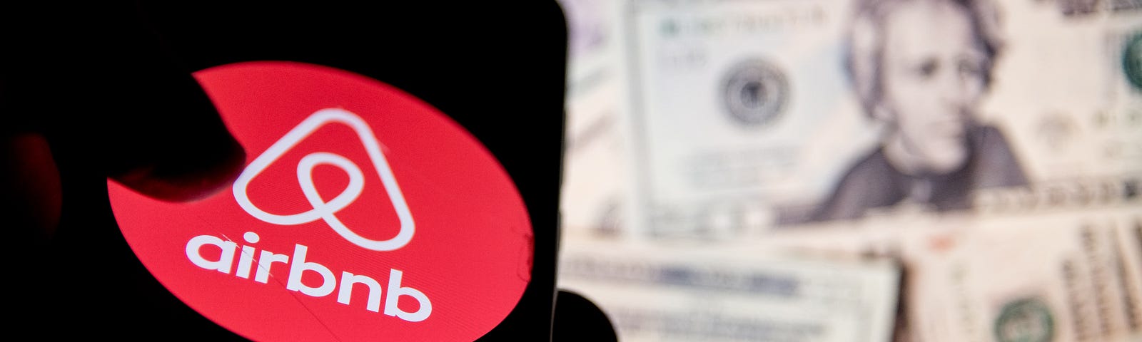 Airbnb logo displayed on a phone screen with bills in the background