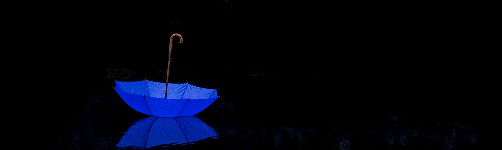 Upside down bright blue umbrella on ground, the rest of image is totally black.