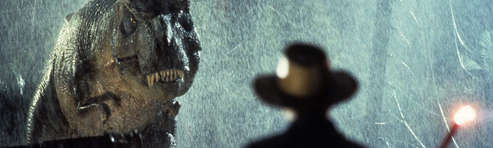 The silhouette of Dr. Allen Grant stands in front of a T. Rex in the rain.