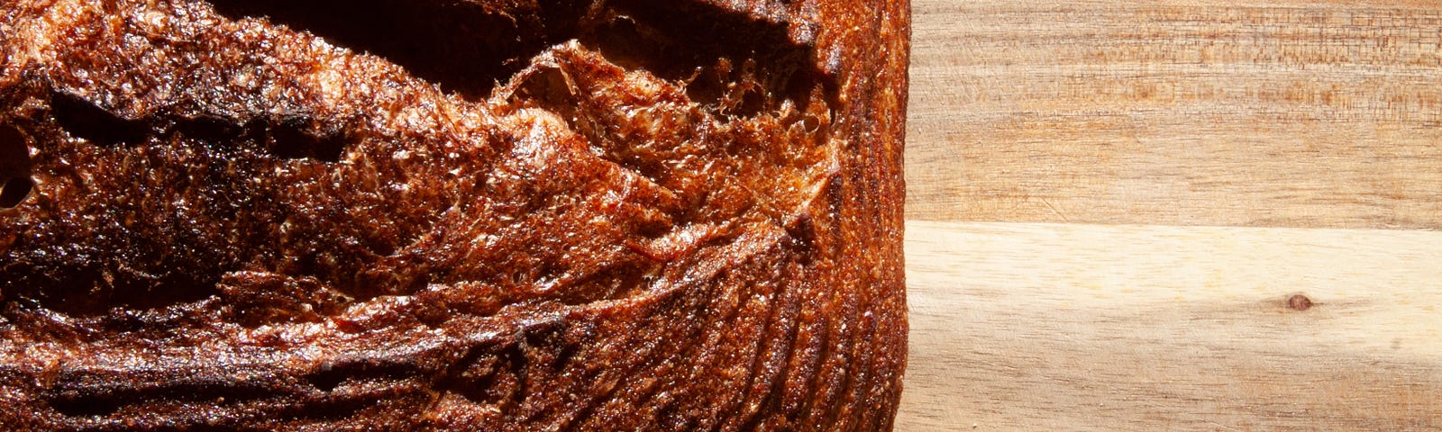 Closeup of a round, dark brown loaf of bread on a wooden surface.