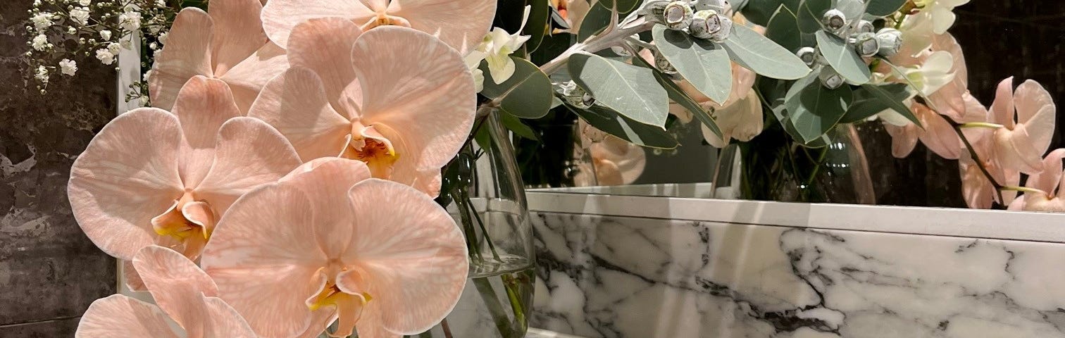 A floral arrangement in soft pastel shades, set on a marble counter top in front of a mirror.