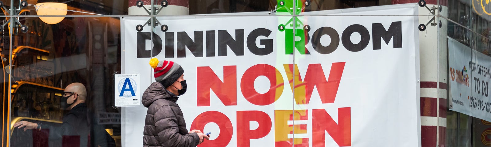 A person walks by a sign that reads, “Dining room now open” outside a restaurant in Times Square.