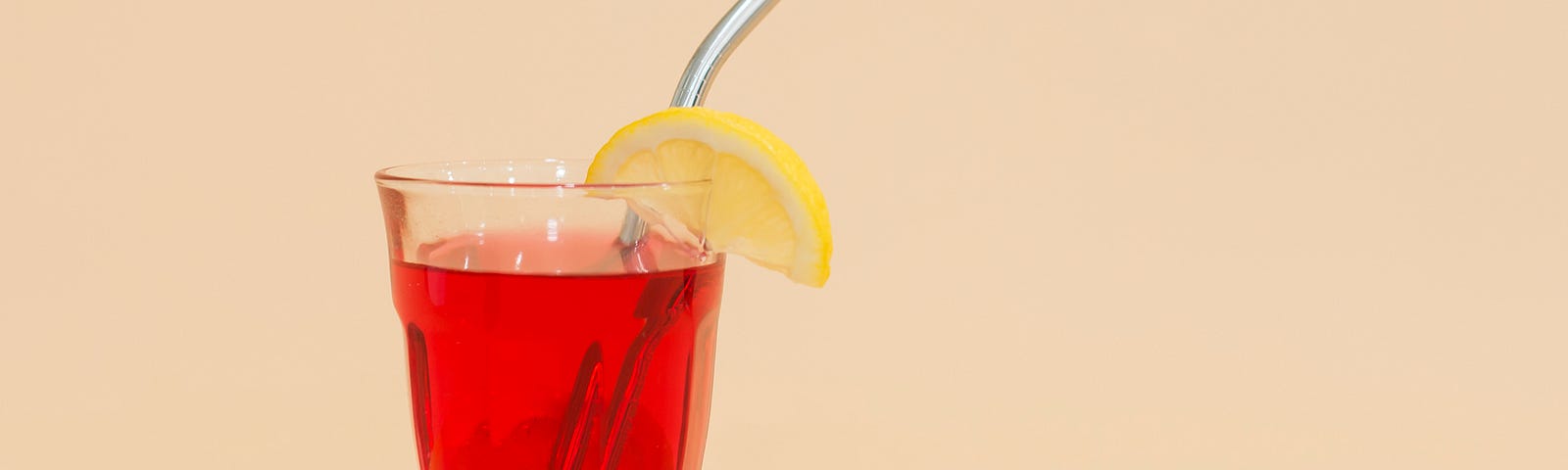 Red drink with lemon wedge and metal straw.