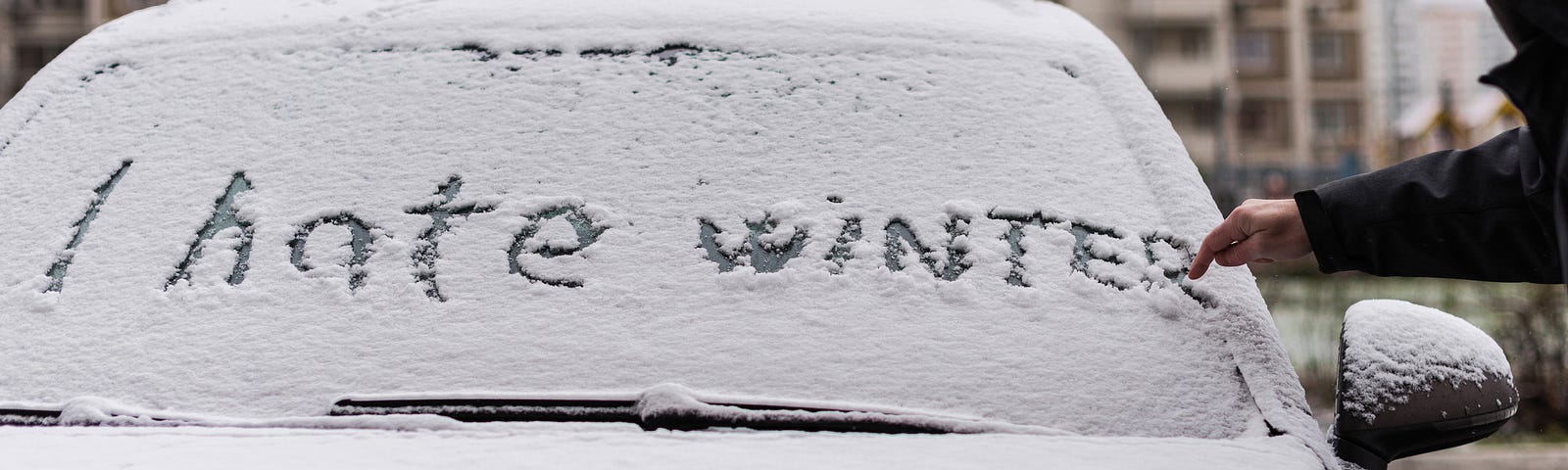 “I hate winter” written on snow covering a car.