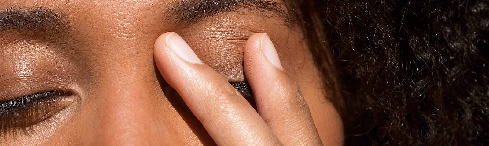 Young Black woman touching her eyelid in stress.