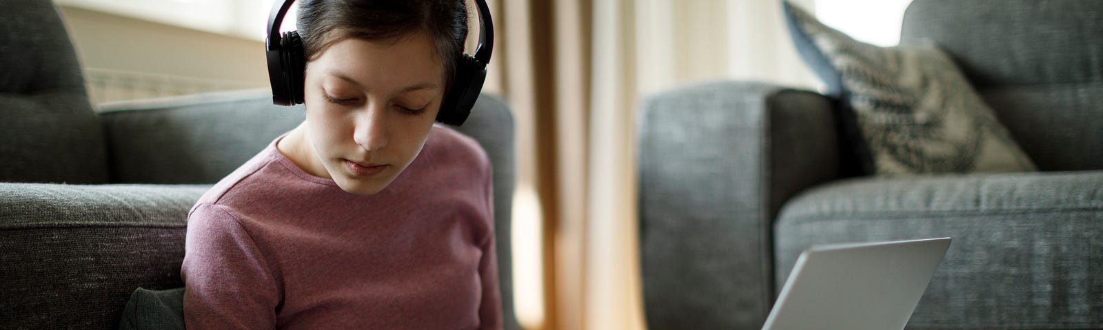 Teenage girl with headphones taking notes during an online class at home.