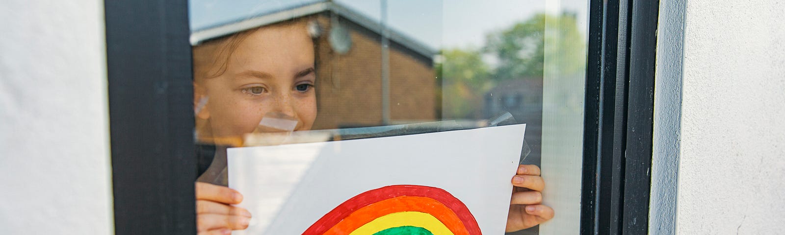 Child putting up a rainbow drawing on their window.