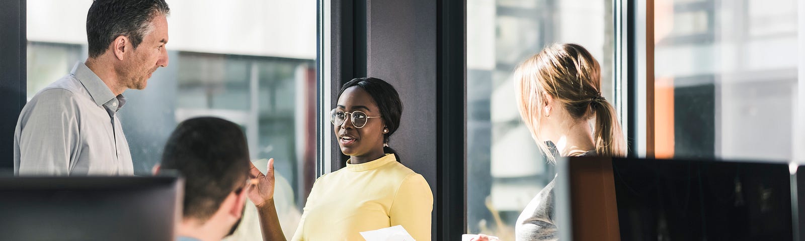 A photo of a Black businesswoman talking to her White colleagues.