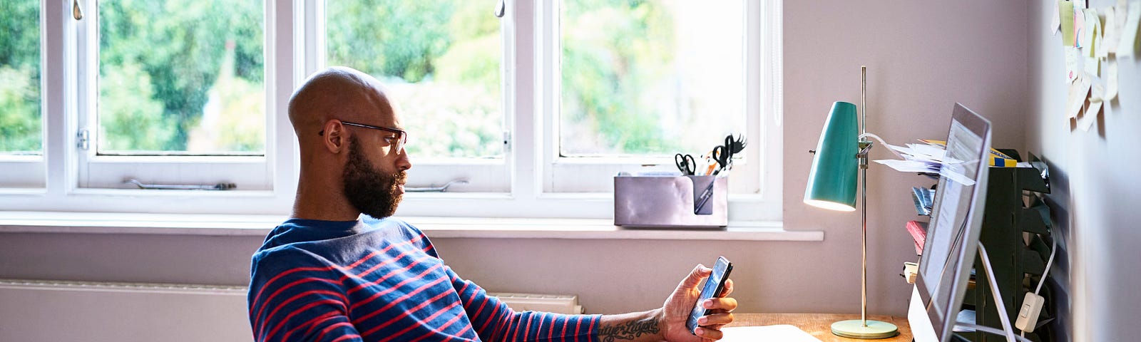 Man looks at his phone while sitting at his desk.