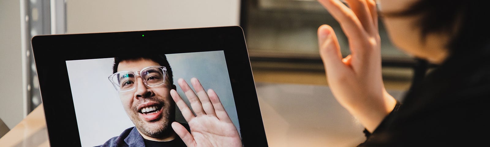 Remote job interview, woman waves to the interviewer through the webcam.