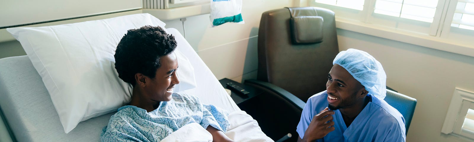 A smiling nurse jokes with a boy patient in a hospital bed.