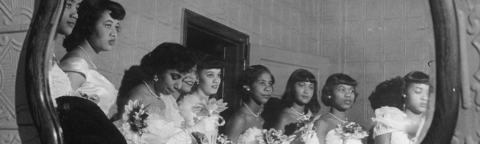 An archival photo of young African American women waiting to go downstairs for their debutante cotillion.