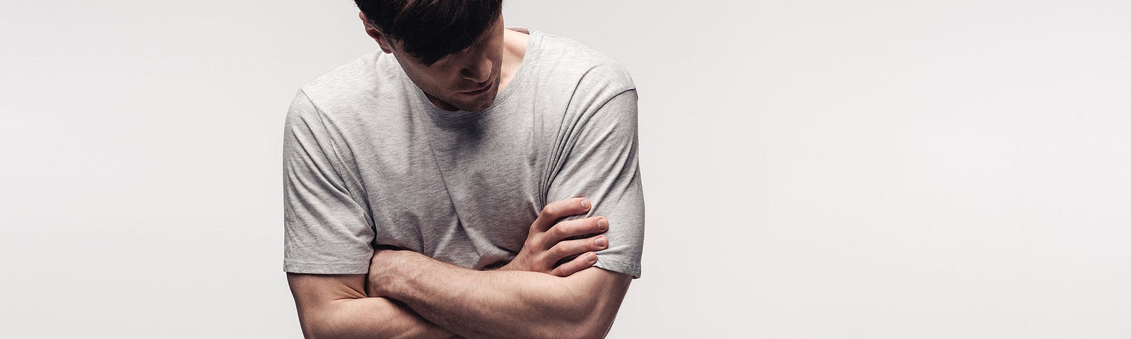 Man looking down with arms crossed and rolling shoulders in