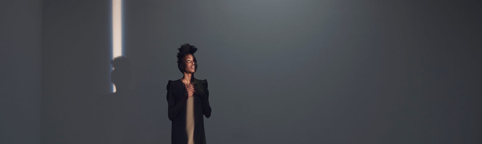 Woman walking in thin light stripe and looking up, in studio with concrete floor