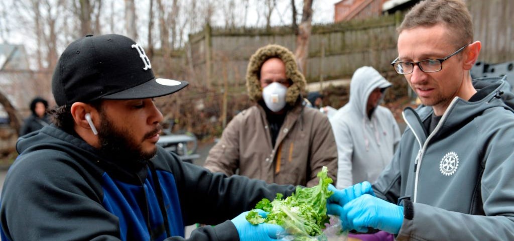 A photo of a group of volunteers gathering lettuce to give to people waiting in line for groceries.