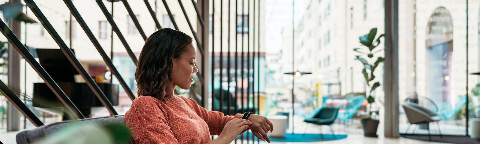 Woman checks her watch to see the time while sitting on the couch.