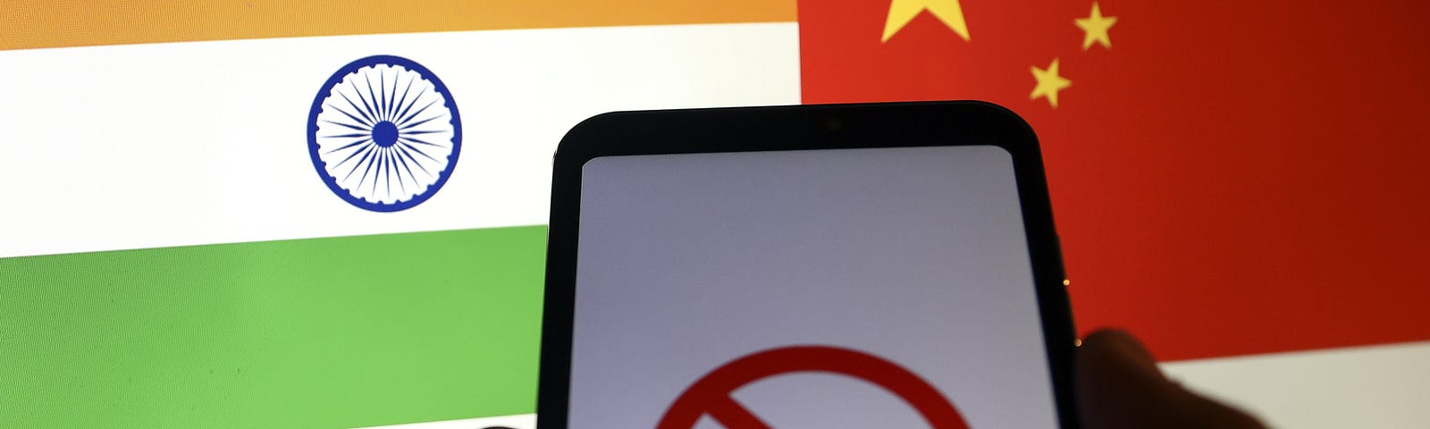 Indian flag and Chinese flag are displayed on a laptop screen behind a smart phone displaying a symbol of “block”