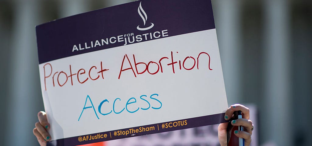 A woman holding up a sign that says “Protest Abortion Access.”