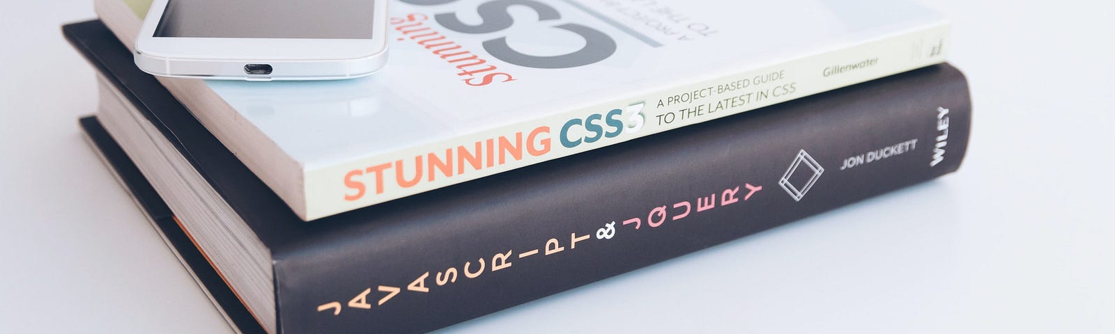 A stack of books on JavaScript and CSS with a phone on top