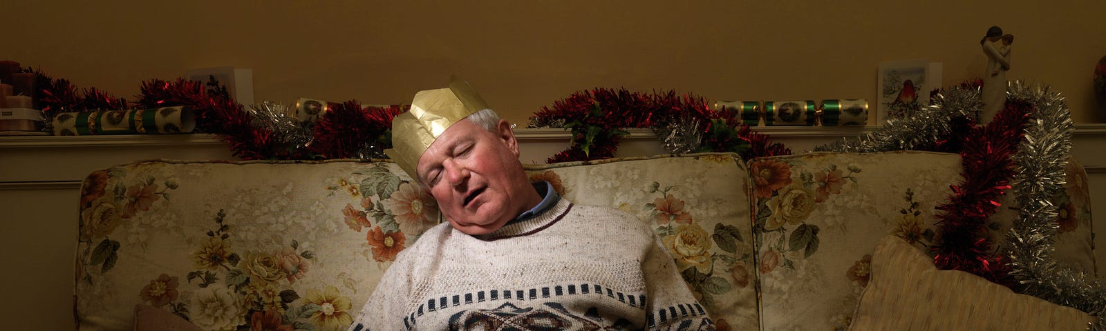 An old man with a gold paper crown hat sleeping on the couch.