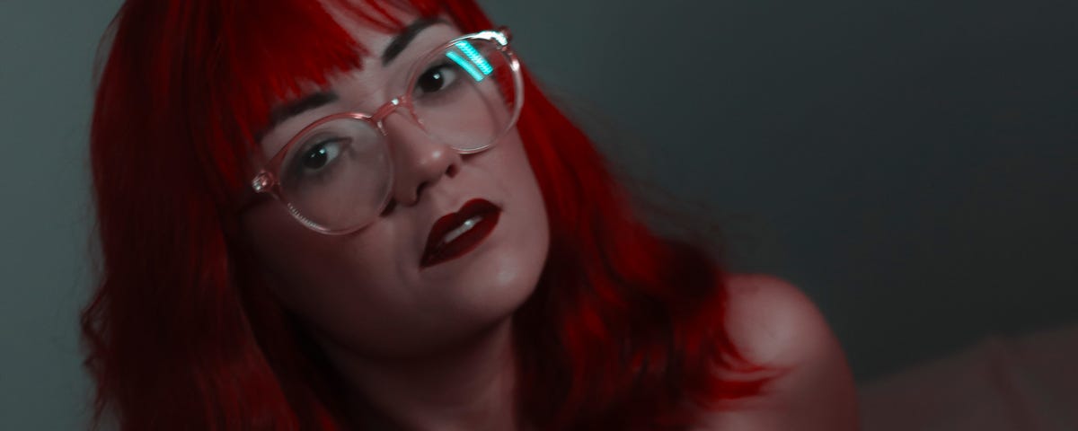 A red haired lady wearing glasses.
