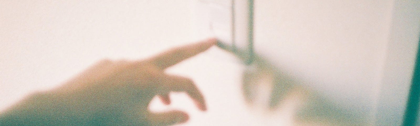 A washed out grainy image of a person touching a light switch.