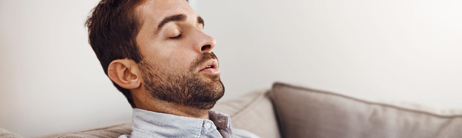 A young man holding his chest in pain while relaxing on a sofa at home.